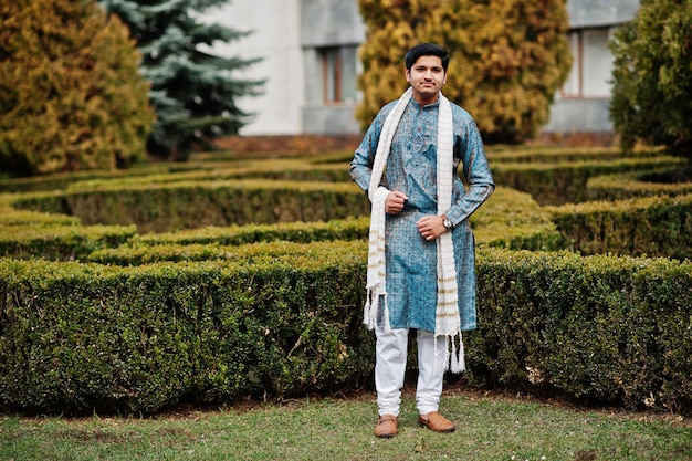 Foto gratuita hombre indio vestido con ropa tradicional con bufanda blanca posada al aire libre contra arbustos verdes en el parque