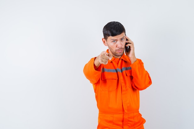 Hombre industrial hablando por teléfono móvil, apuntando en vista frontal uniforme.