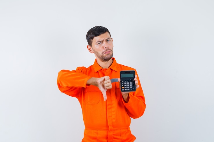 Foto gratuito hombre industrial sosteniendo la calculadora, mostrando el pulgar hacia abajo en uniforme y mirando disgustado, vista frontal.