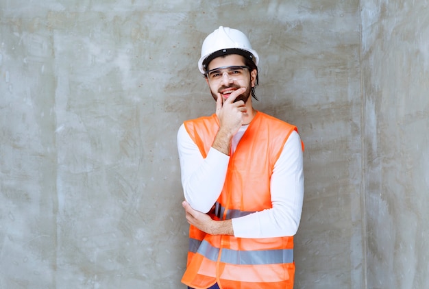 El hombre ingeniero con casco blanco y anteojos protectores parece confundido y pensativo.