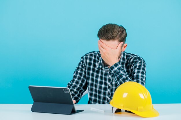 Foto gratuita el hombre ingeniero está cubriendo la cara sosteniendo la mano en la frente sobre fondo azul.