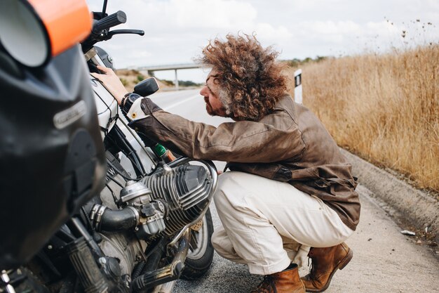 El hombre intenta arreglar la moto al costado de la carretera