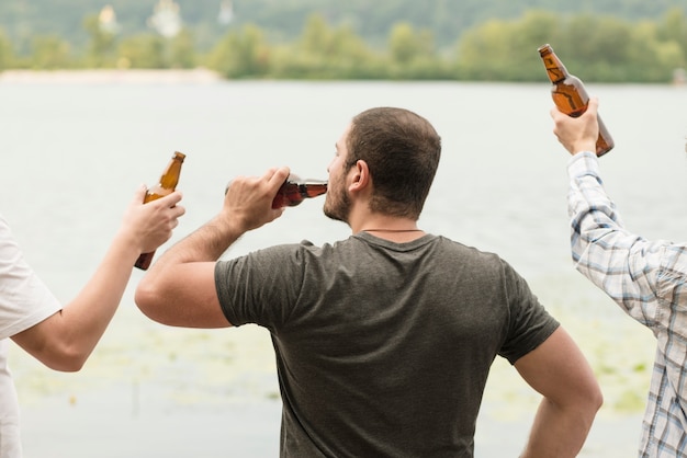 Hombre irreconocible bebiendo cerveza cerca del agua con amigos