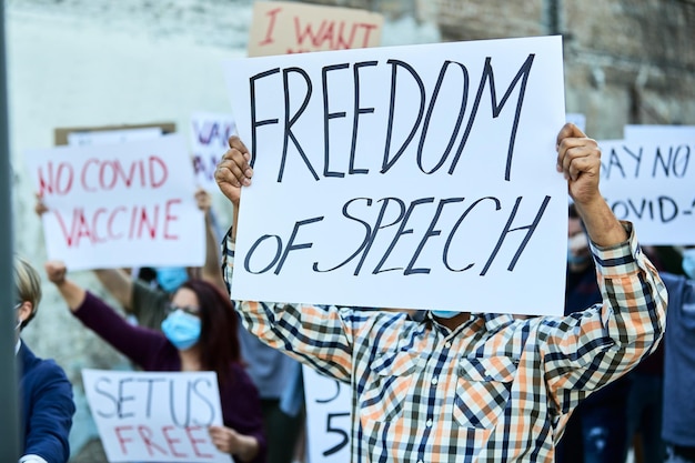 Hombre irreconocible con pancarta de libertad de expresión marchando con un grupo de personas en una protesta durante la pandemia del coronavirus