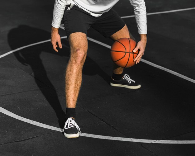 Hombre irreconocible rebotando baloncesto en la cancha