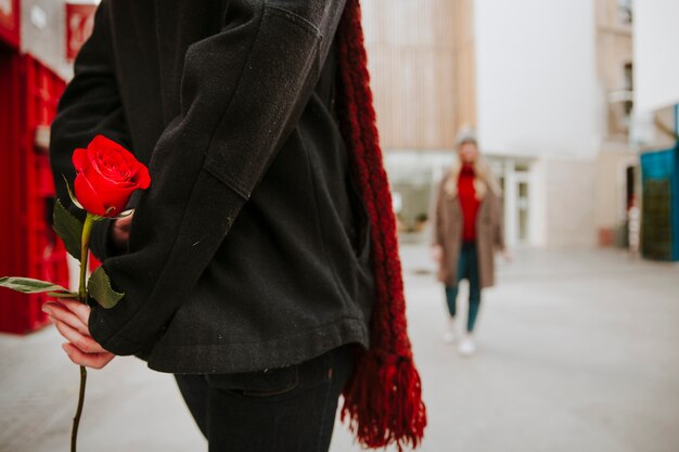 Hombre irreconocible con rosa roja esperando mujer