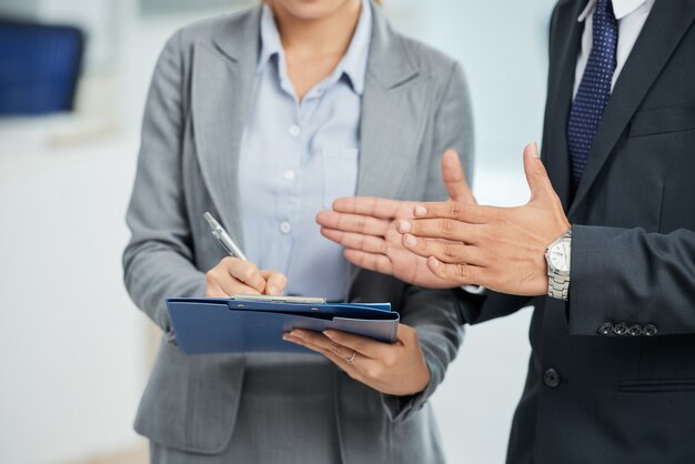 Hombre irreconocible en traje gesticulando y mujer tomando notas