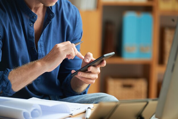 Hombre irreconocible vestido informalmente usando un teléfono inteligente en el trabajo en la oficina