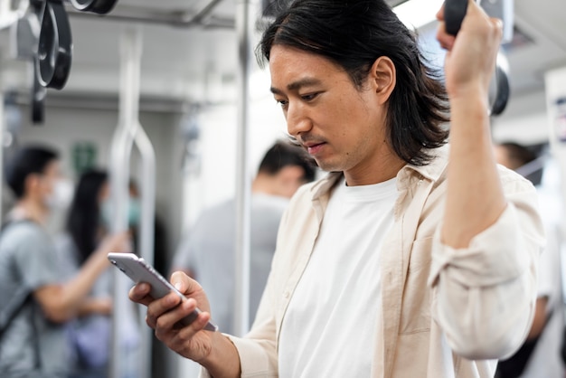 Hombre japonés desplazándose en su teléfono mientras está en el tren