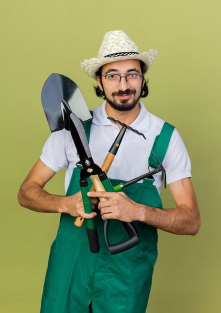 Foto gratuita hombre jardinero complacido en gafas ópticas con sombrero de jardinería tiene herramientas de jardín
