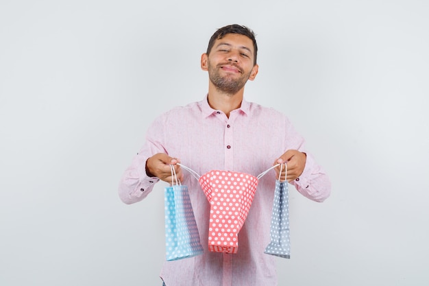 Hombre joven abriendo una bolsa de papel en camisa y mirando contento, vista frontal.