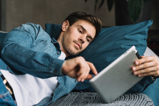 Hombre joven acostado de lado sobre la cama mirando tableta digital