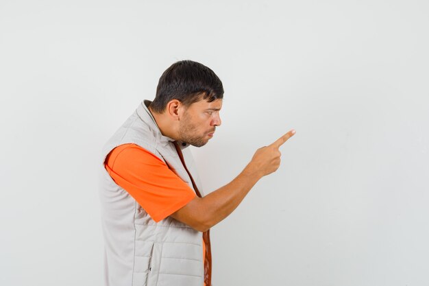 Hombre joven advirtiendo a alguien con el dedo en la camiseta, chaqueta y mirando nervioso. .