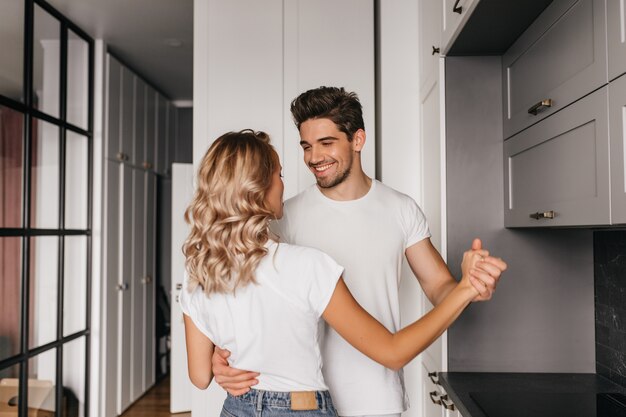 Hombre joven alegre que abraza suavemente a su novia. Pareja bailando en la cocina en la mañana del fin de semana.