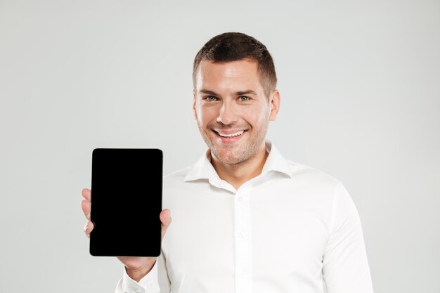 Hombre joven alegre que muestra la pantalla de la tableta.