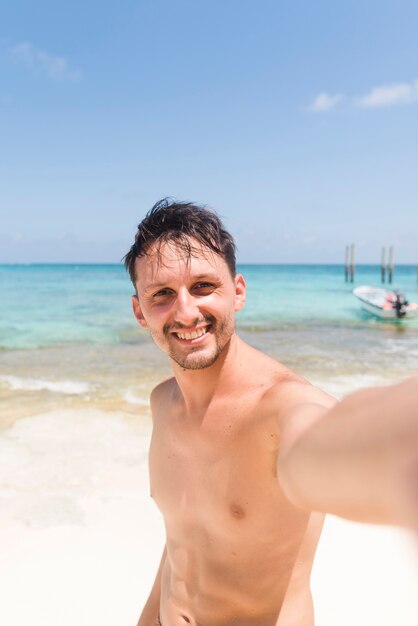 Hombre joven alegre tomando selfie en la playa