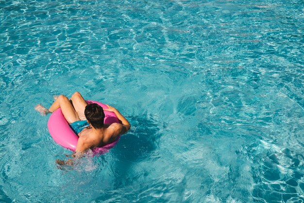 Hombre joven en anillo flotador en piscina