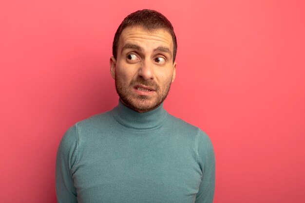 Hombre joven ansioso mirando al lado aislado en la pared rosa