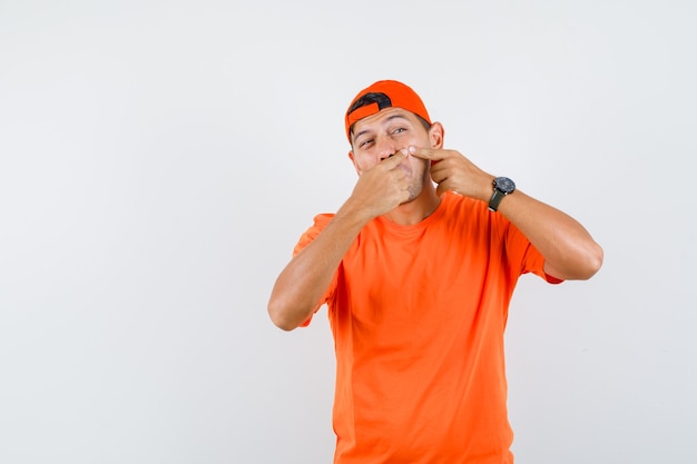 Hombre joven apretando su grano en la mejilla en camiseta naranja y gorra