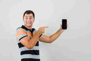 Foto gratuita hombre joven apuntando al teléfono en camiseta y mirando feliz. .