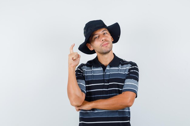Hombre joven apuntando hacia arriba en camiseta, sombrero y mirando confiado. vista trasera.