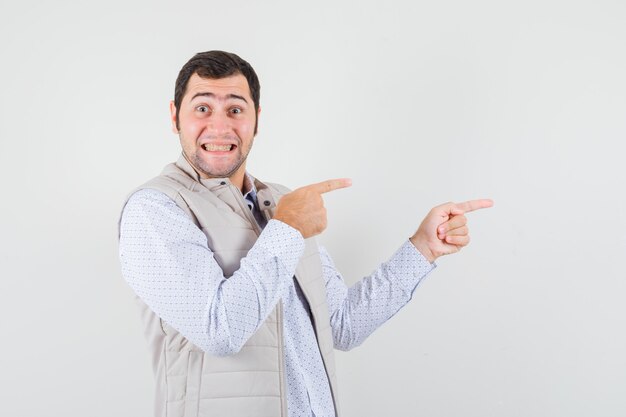 Hombre joven apuntando a la derecha con los dedos índices en chaqueta beige y con aspecto optimista. vista frontal.