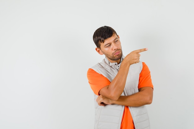 Foto gratuita hombre joven apuntando hacia el lado en camiseta, chaqueta y aspecto sensato.