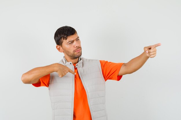 Hombre joven apuntando a sí mismo y lejos en camiseta, vista frontal de la chaqueta.