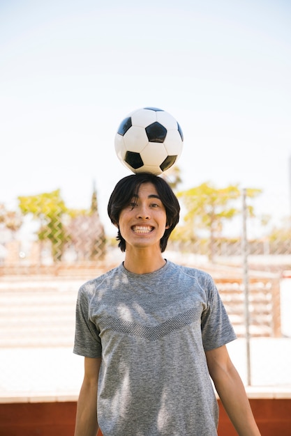 Foto gratuita hombre joven asiático que balancea el balón de fútbol en la cabeza