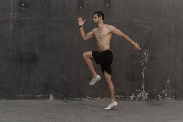 Hombre joven atleta, torso desnudo, corriendo contra una pared gris