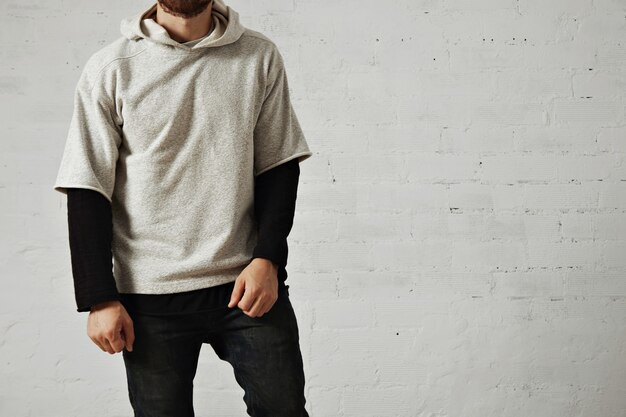 Hombre joven atlético tranquilo relajado con una barba vistiendo jeans negros, camiseta negra de manga larga y una cómoda sudadera con capucha gris jaspeado liso aislado en blanco