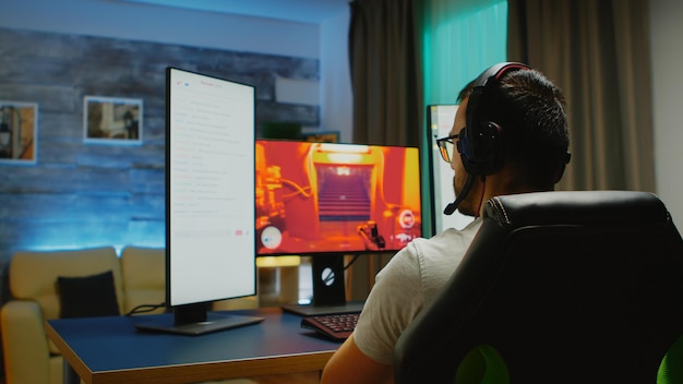 Hombre joven con auriculares hablando por chat mientras juega juegos de disparos en PC potente