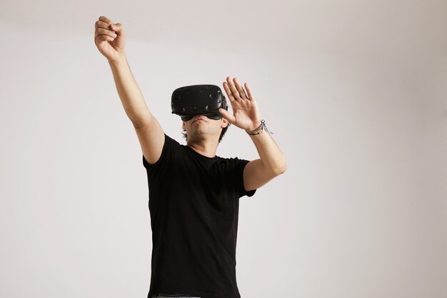 Un hombre joven con auriculares VR vistiendo una camiseta de algodón negro liso interactuando con su entorno aislado en blanco