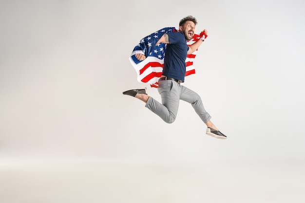 Hombre joven con bandera de los Estados Unidos de América saltando aislado en blanco studio.