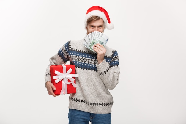 Hombre joven con barba sosteniendo una caja de regalo de navidad y dinero en blanco