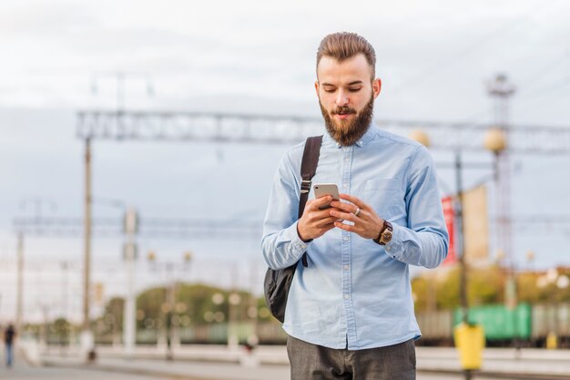 Hombre joven con barba usando teléfono celular