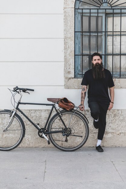 Hombre joven barbudo de pie cerca de la bicicleta