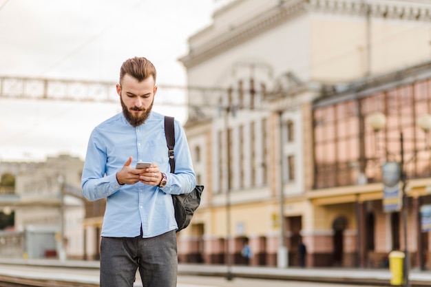 Hombre joven barbudo que usa el teléfono móvil en la estación de tren