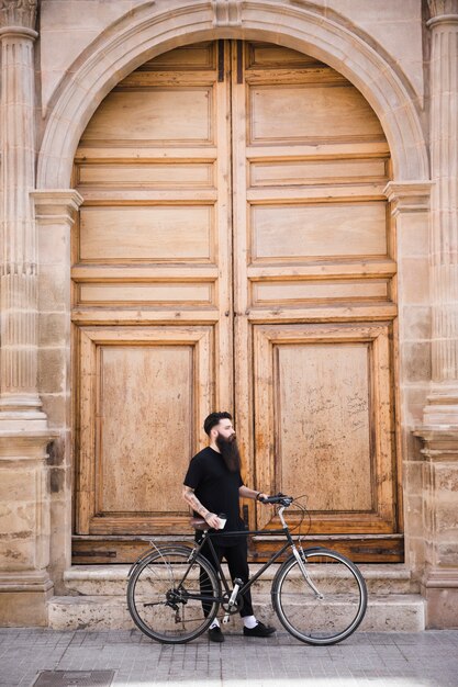 Hombre joven con bicicleta de pie cerca de la puerta cerrada de la vendimia