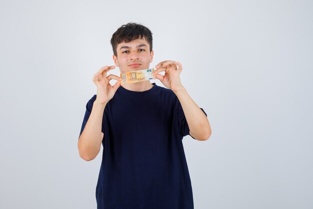 Hombre joven con billete de euro en camiseta negra y mirando confiado. vista frontal.