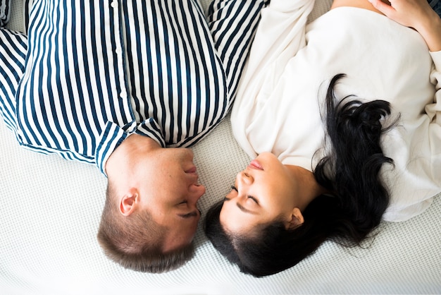 Hombre joven y bonita mujer étnica durmiendo en la cama cara a cara