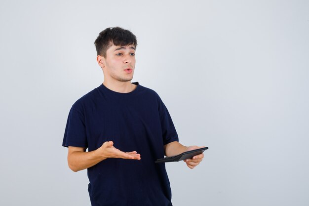 Hombre joven con calculadora en camiseta negra y mirando desconcertado, vista frontal.