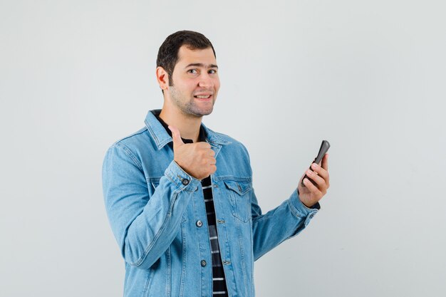 Hombre joven con calculadora, mostrando el pulgar hacia arriba en camiseta, chaqueta y mirando jovial.