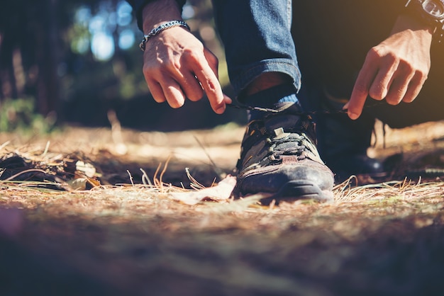 El hombre joven del caminante ata los cordones en su zapato durante un día de fiesta backpacking en bosque.