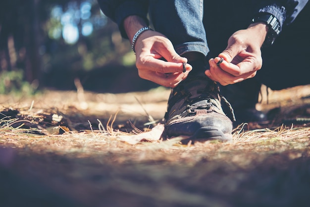 El hombre joven del caminante ata los cordones en su zapato durante un día de fiesta backpacking en bosque.