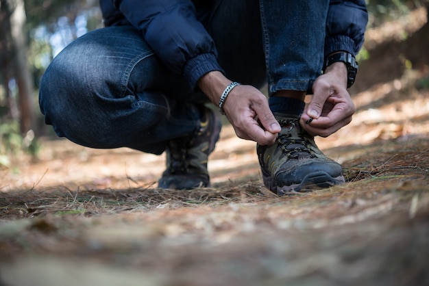 El hombre joven del caminante ata los cordones en su zapato durante un día de fiesta backpacking en bosque.