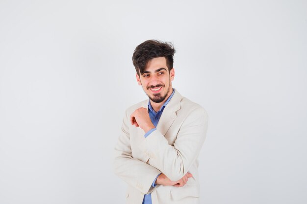 Hombre joven con camisa azul y chaqueta de traje blanco de pie en pose de pensamiento y mirando feliz