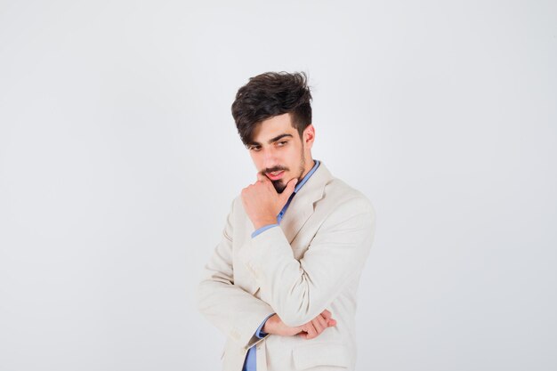 Hombre joven con camisa azul y chaqueta de traje blanco de pie en pose de pensamiento y mirando pensativo
