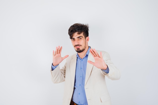 Hombre joven con camisa azul y chaqueta de traje blanco que muestra señales de alto y parece feliz