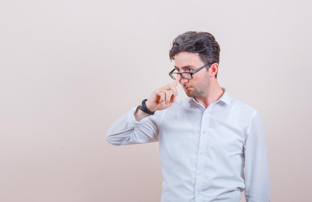 Hombre joven con camisa blanca ajustando sus gafas y mirando pensativo